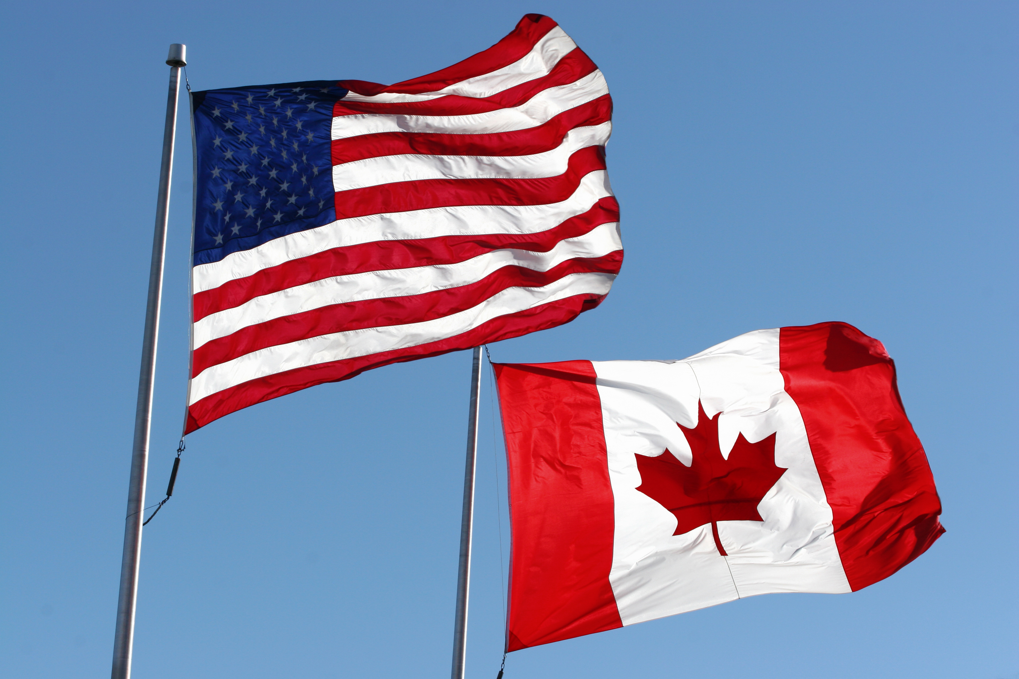 The Canadian and American flags next to each other on a sky background